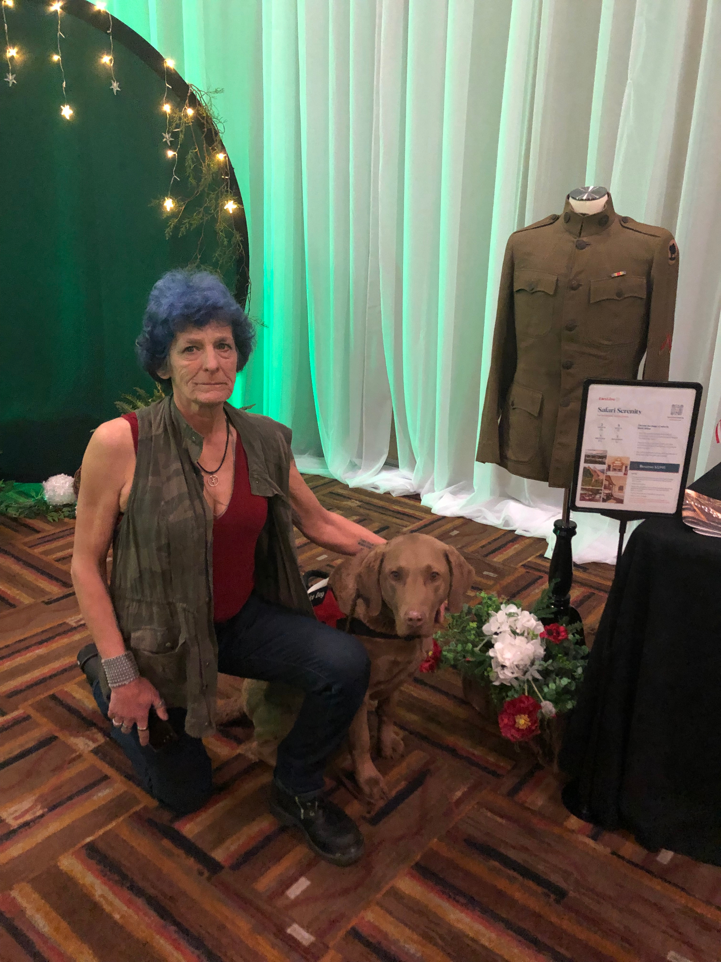 A veteran kneeling with her service dog beside a historic military uniform display